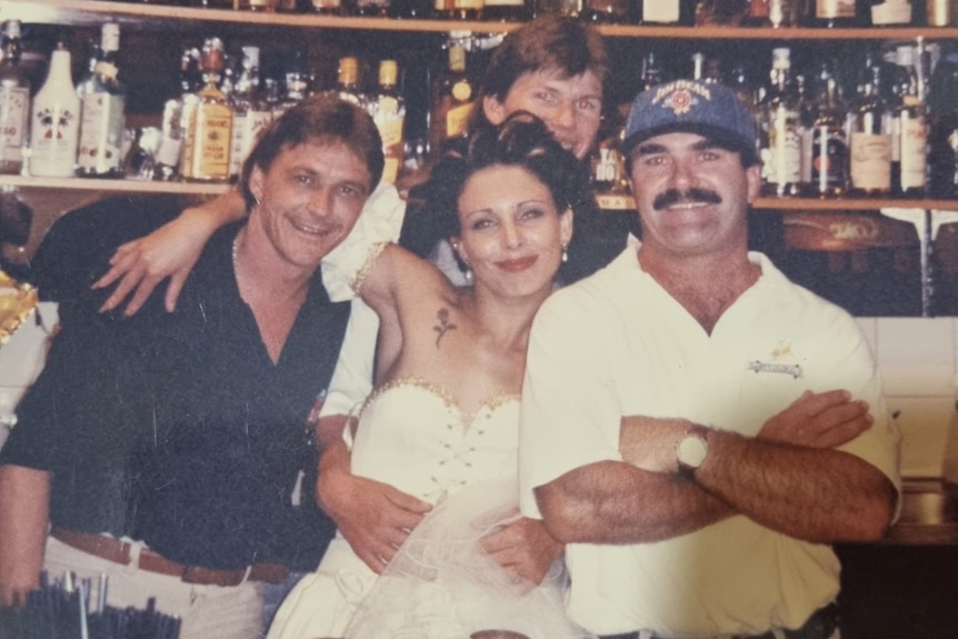 Older photo of three men and a woman standing behind a bar