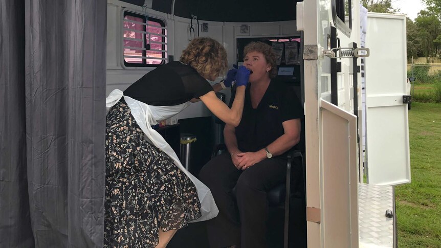 A doctor swabs a woman's mouth. The test is being done inside a converted horse float.