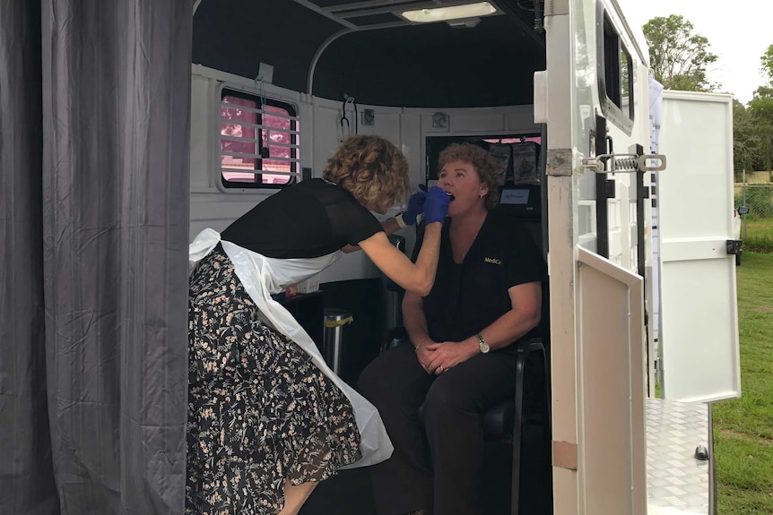 A doctor swabs a woman's mouth. The test is being done inside a converted horse float.