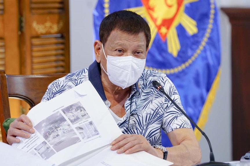 Philippines President Rodrigo Duterte holds documents and wears a mask.