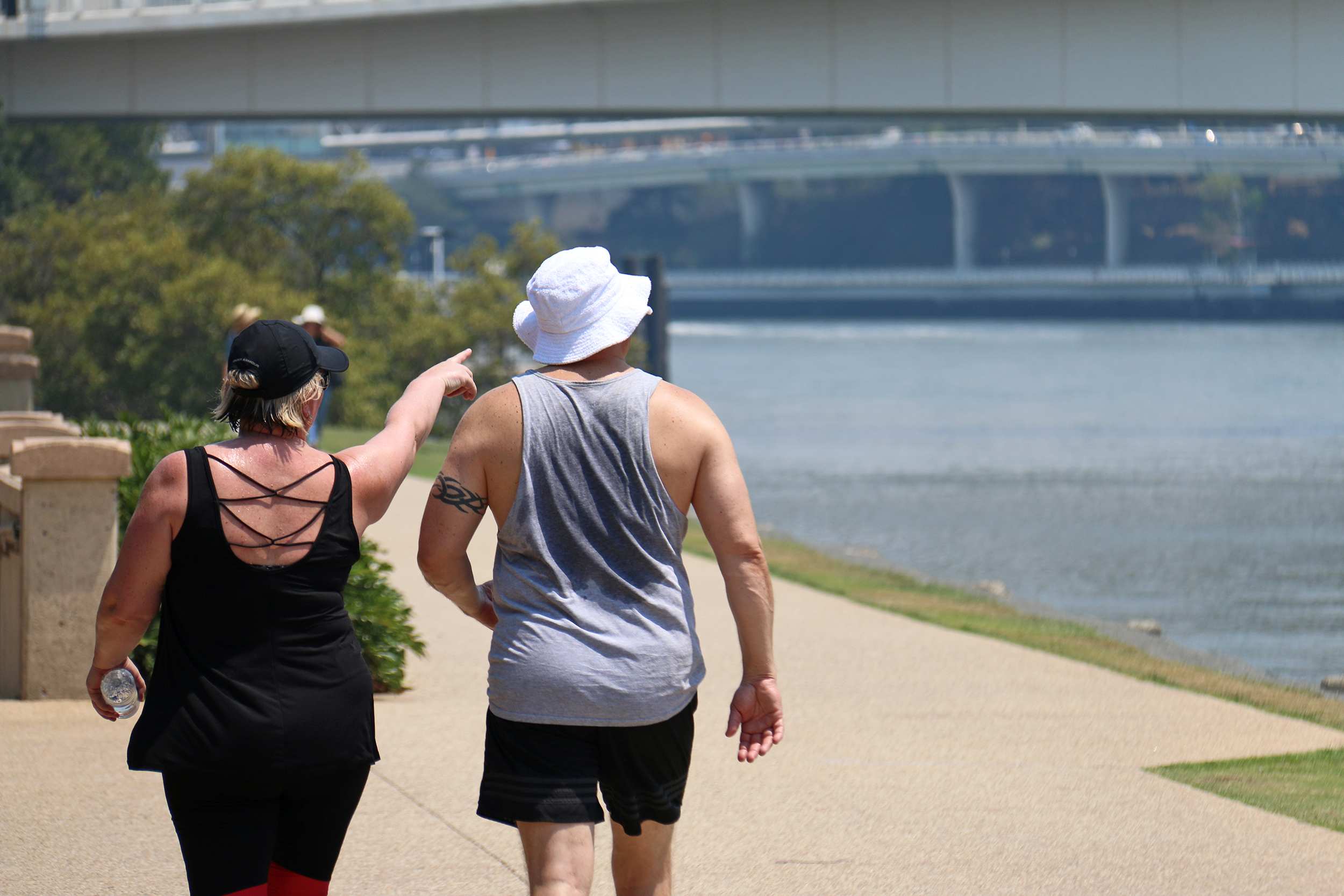 A woman and a man whose singlet is drenched with sweat walk along the Brisbane River.