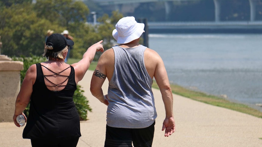 A woman and a man whose singlet is drenched with sweat walk along the Brisbane River.