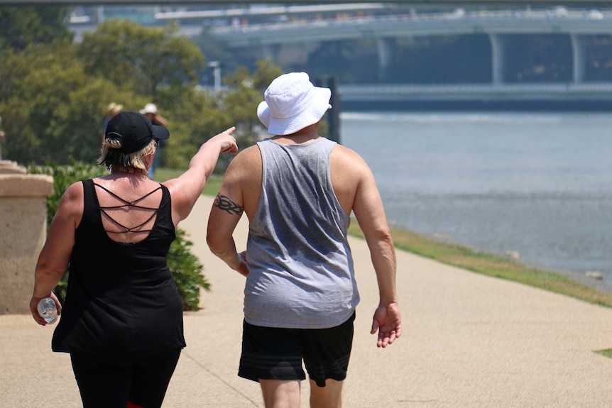 A woman and a man whose singlet is drenched with sweat walk along the Brisbane River.