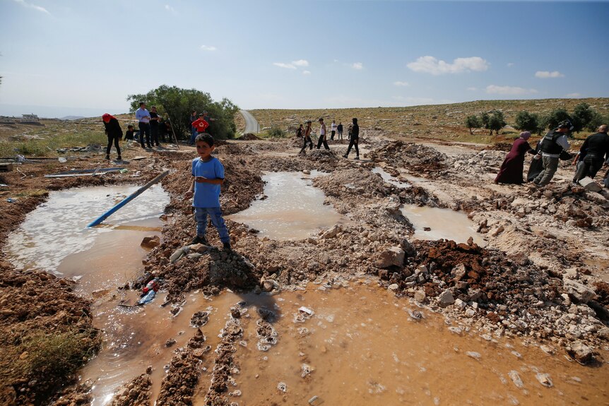 Boy stands on mud and rubble of where a school once stood, demolished by Israeli forces.