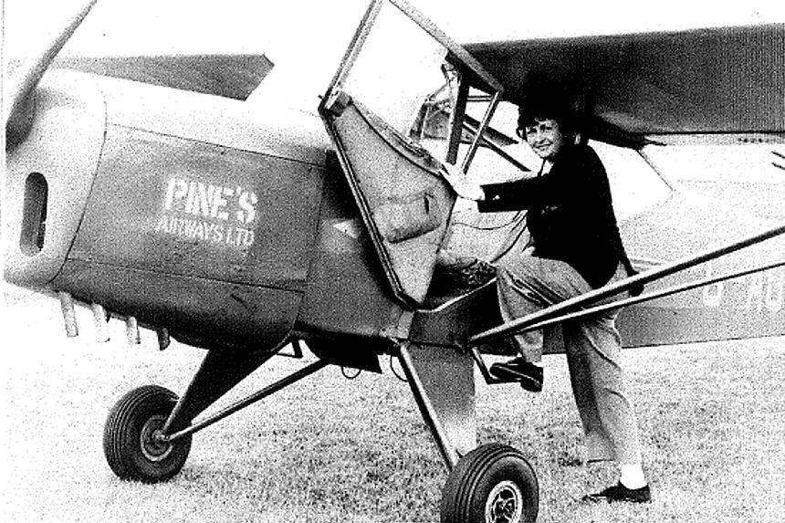 Black and white photo of a woman with a small plane, she has one leg up on the side of the plane