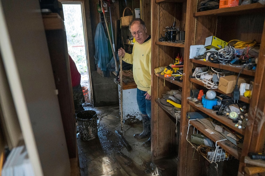 A man in a flooded house standing next to a bookshelf