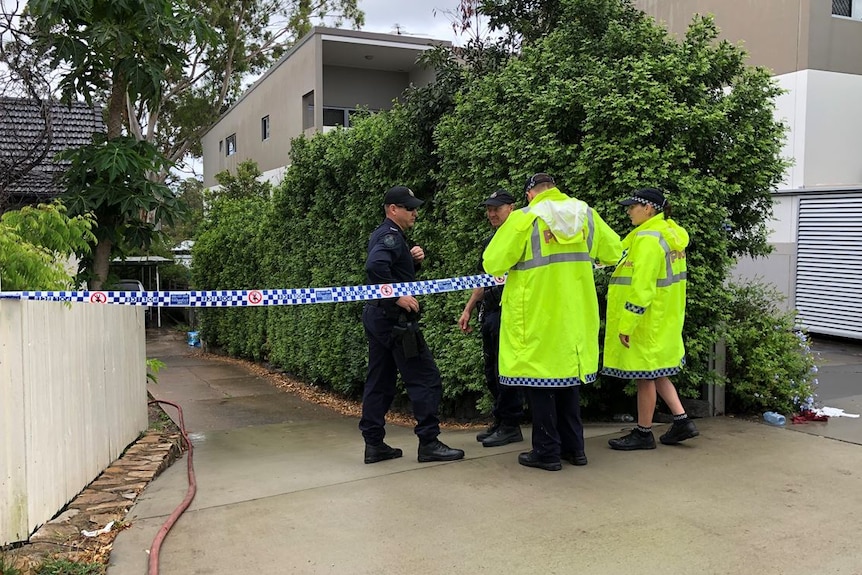 Two police in high viz coats and two other officers stand on a driveway next to crime scene tape