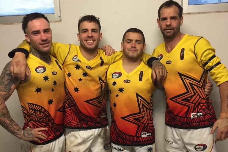 Four AFL players with their hands around one another smiling for a photo in their team uniform