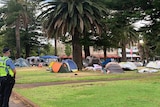 A police officer stands to one side as campers pack up.