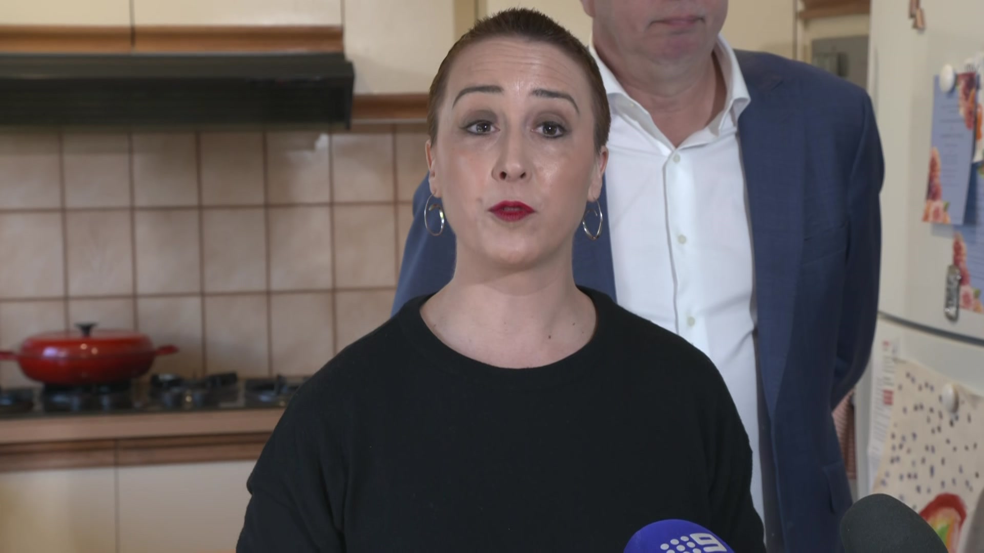 A woman with a shaved head stands in the kitchen of a home.