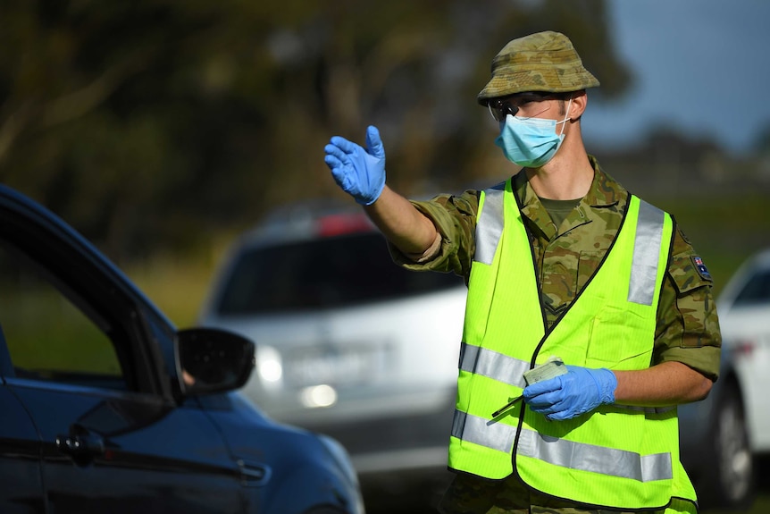 An army officer in a high-vis vest, gloves and a mask directs traffic.