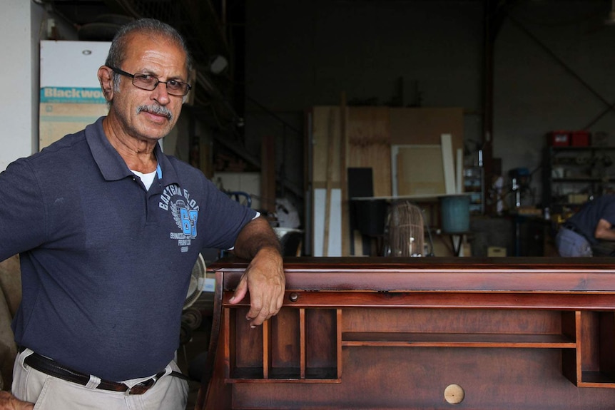 Walter Pereirra stands, leaning on the antique roller desk he has finished restoring.