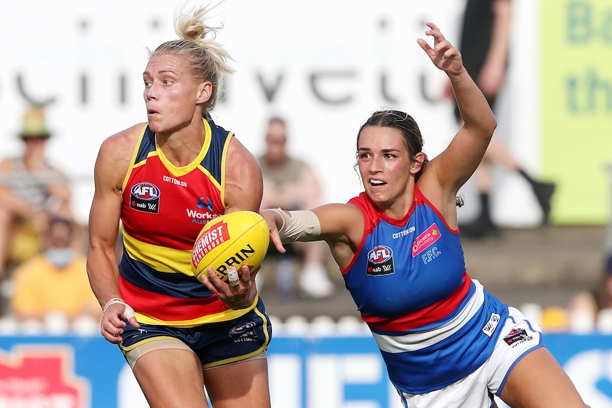 An Adelaide Crows AFLW player looks to handball while under pressure from a Western Bulldogs opponent.