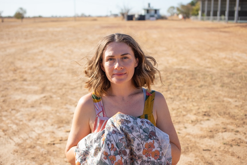 A woman stands in the centre of the frame, looking up at the camera and holding a piece of fabric.