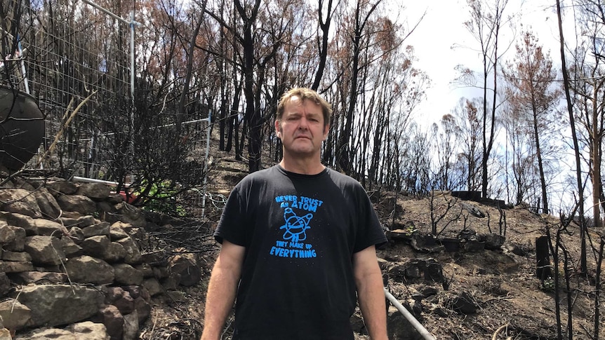 David O'Brien stands in front of burnt out trees.