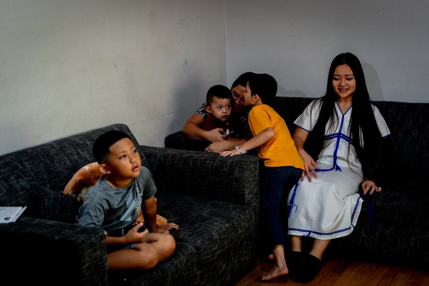 Small family of boys gather on a small couch with teenage girl and mother.