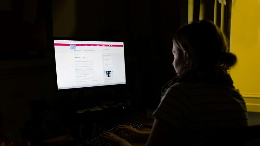 Woman sitting in dark room looking at Crime Stoppers website on computer