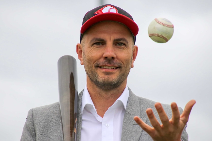 Perth Heat general manager Steve Nelkovski holding a baseball bat while a ball is in mid-air.