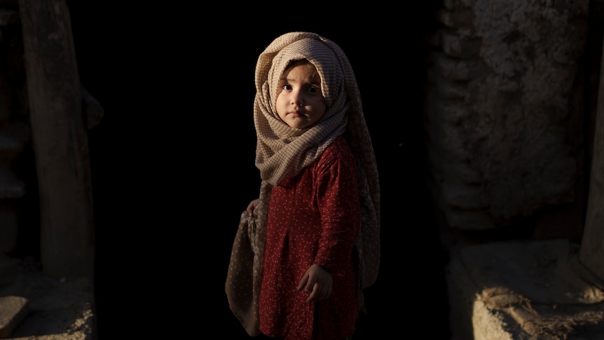 A young girl in colourful dress looks at the camera. 