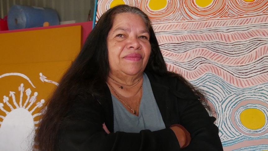 A woman stands thoughtfully in front of colourful artwork