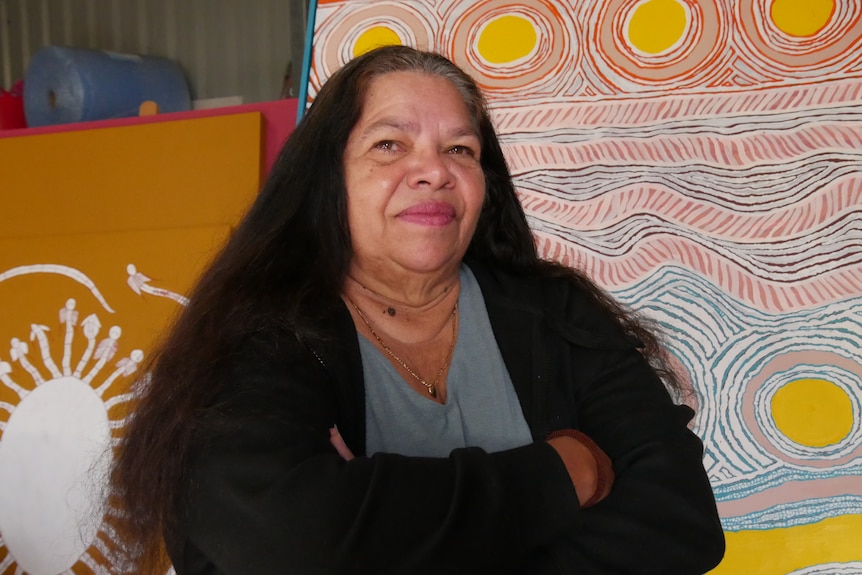 A woman stands thoughtfully in front of colourful artwork