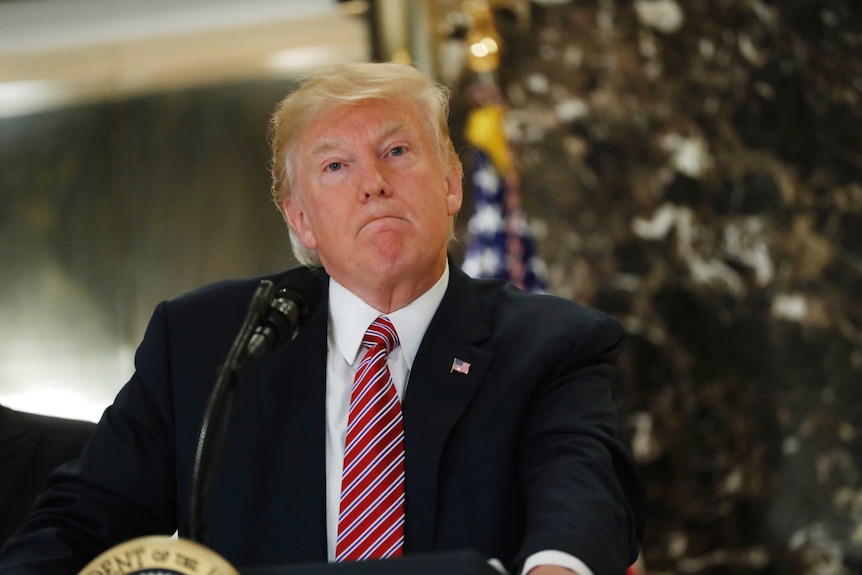 US President Donald Trump stands with his lips pressed together at podium