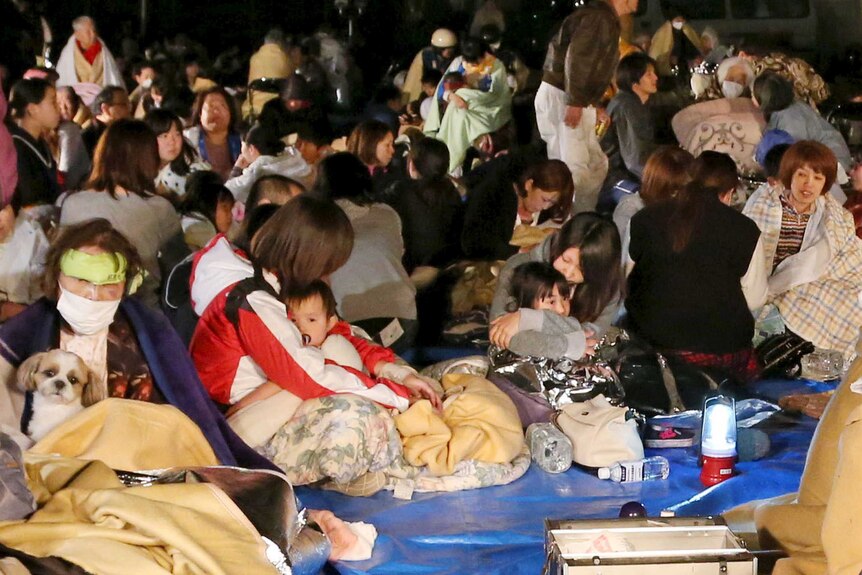 large crowd of people sit on the floor with blankets wrapped around after escaping earthquake