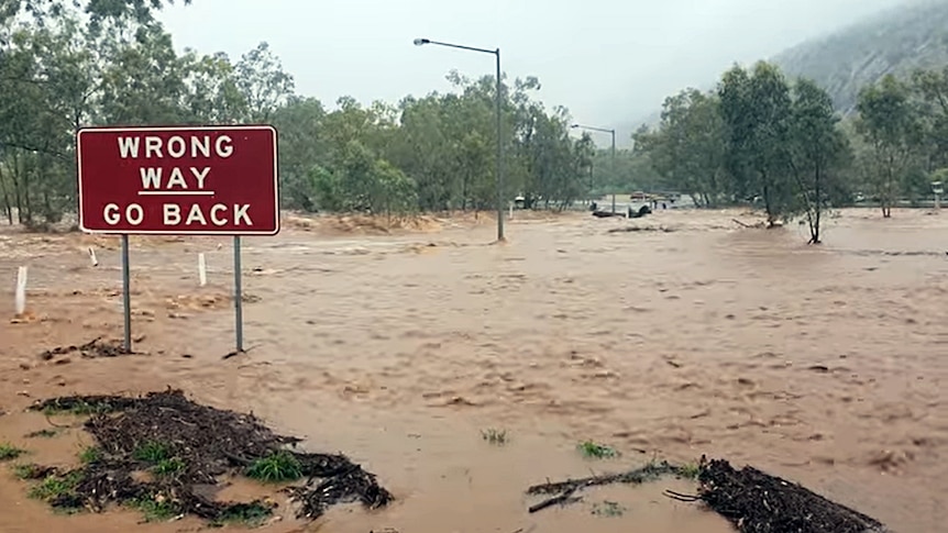 WRONG WAY GO BACK sign in front of rapidly flowing brown floodwaters