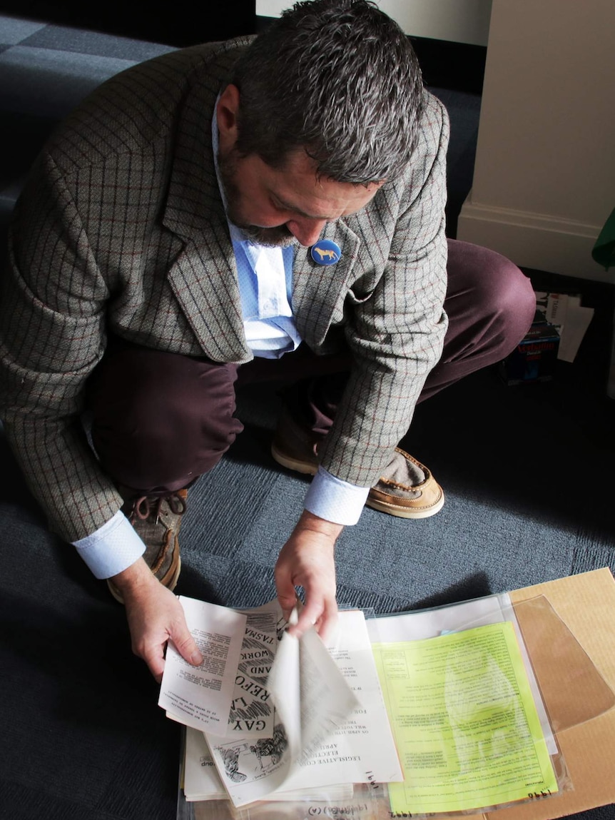 Rodney Croome crouches and sorts through a folder of paper items.