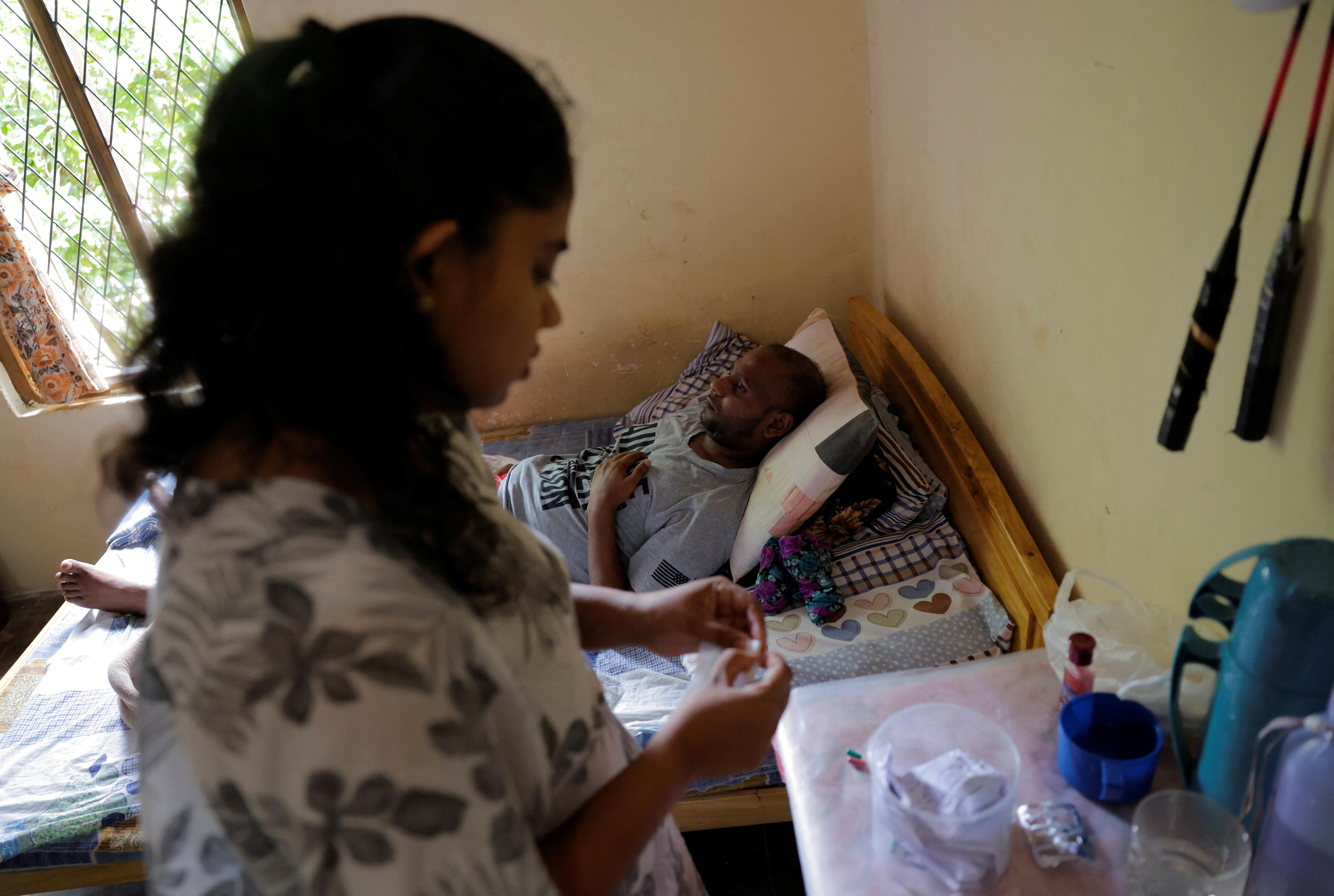 a woman prepares medication for a man laying in pain on a bed