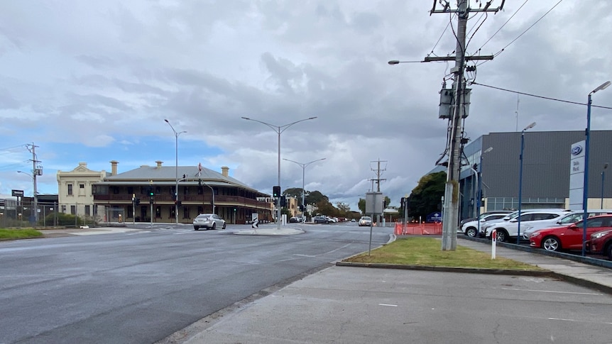 An intersection in a country town with a historic pub on one corner and a car dealership on the other.