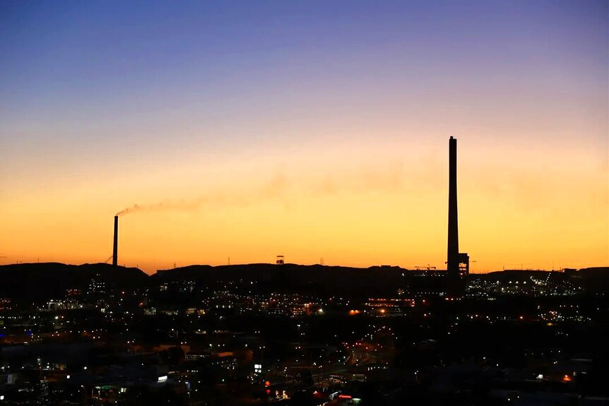 Smoke stacks in silhouette as the sun sets over an outback city.