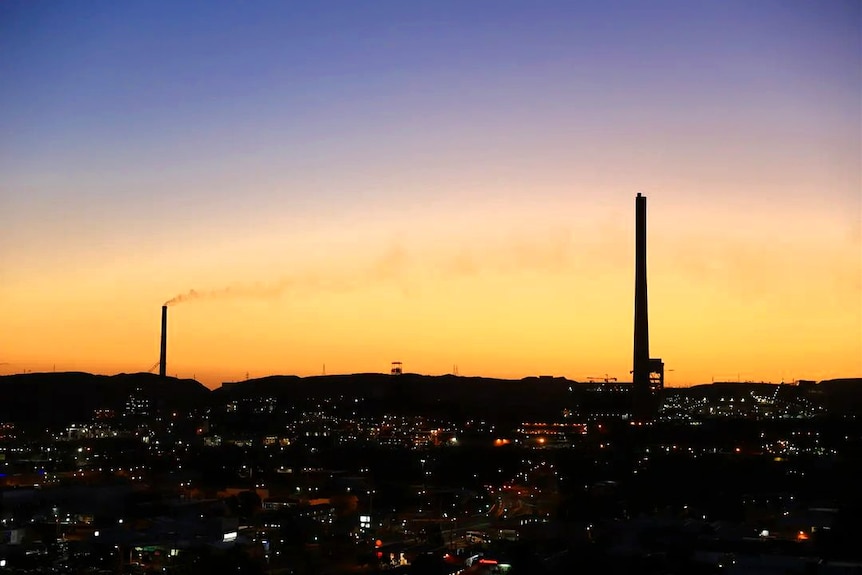 Pilas de humo en silueta mientras el sol se pone sobre una ciudad del interior.