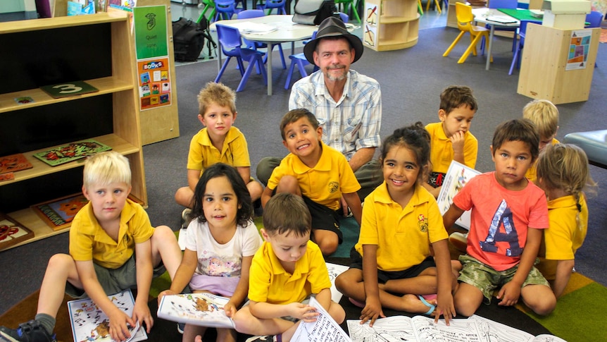 A man in a hat sits behind students in a classroom