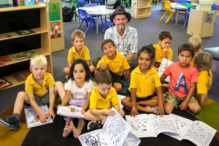 A man in a hat sits behind students in a classroom