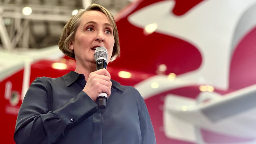 Qantas CEO Vanessa Hudson stands in front of a Qantas plane in a hanger, with the Flying Kangaroo logo prominently visible.