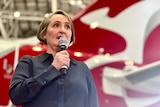 Qantas CEO Vanessa Hudson stands in front of a Qantas plane in a hanger, with the Flying Kangaroo logo prominently visible.