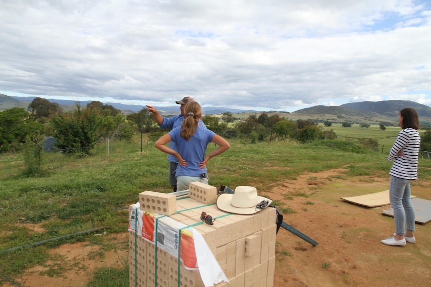 A family stand around a building site overlooking a rural valley. 