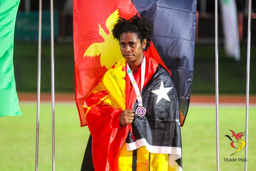 Para-athlete Dorna Longbut has a Papua New Guinea flag draped over her shoulders and a gold medal around her neck. 