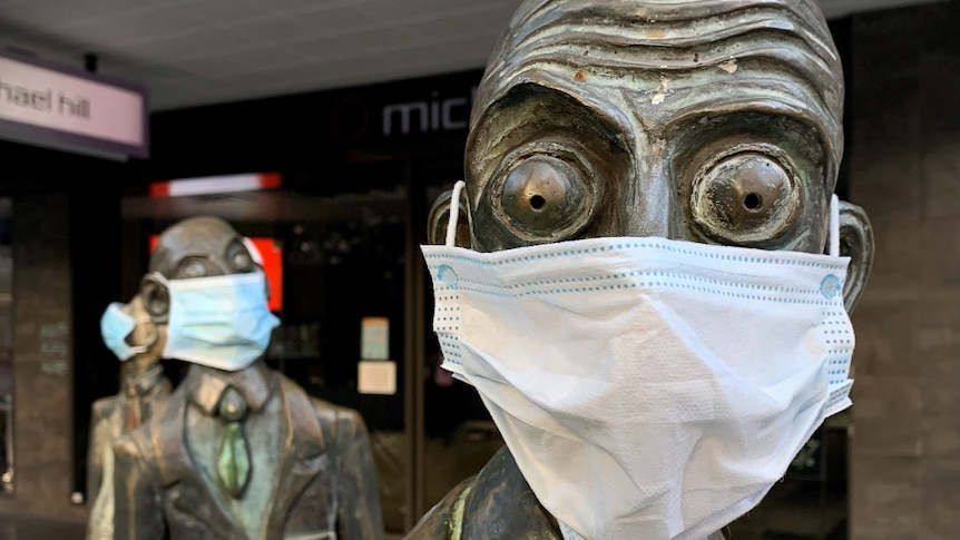 A close up of a bronze sculpture of a businessman in Melbourne with bulging eyes, wearing a blue surgical face mask.