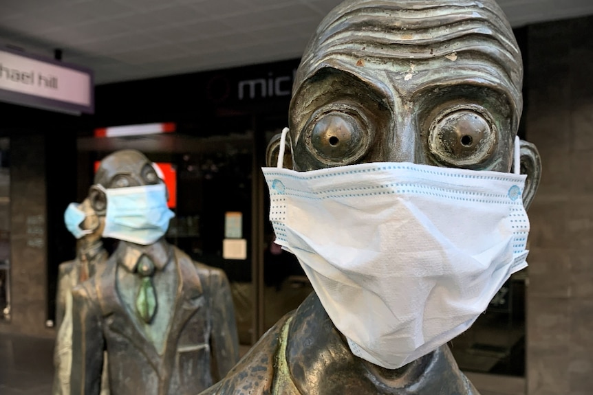 A close up of a bronze sculpture of a businessman in Melbourne with bulging eyes, wearing a blue surgical face mask.