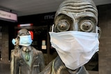 A close up of a bronze sculpture of a businessman in Melbourne with bulging eyes, wearing a blue surgical face mask.