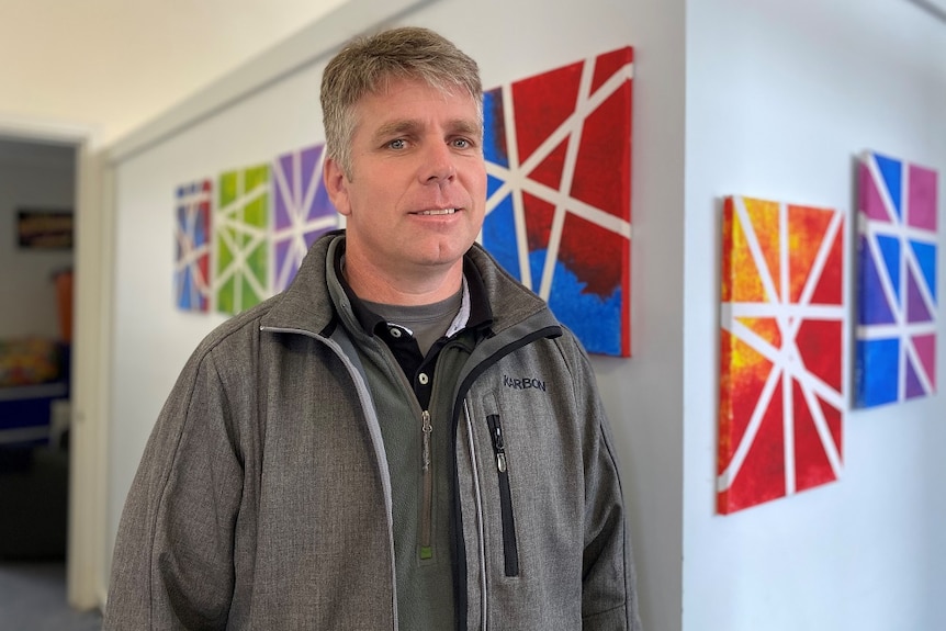 A man standing in front of a wall with colourful canvasses.