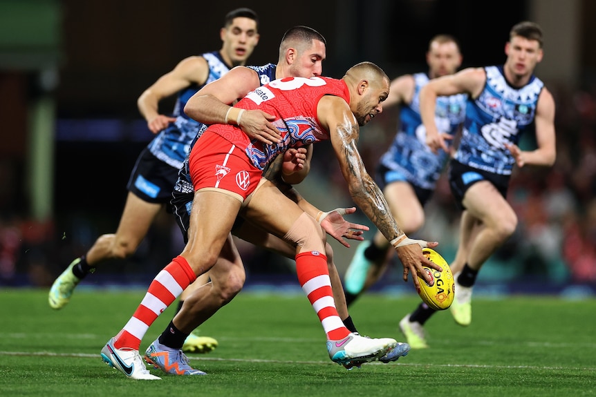 Lance Franklin bends over to pick the ball up as Jacob Weitering puts pressure on him