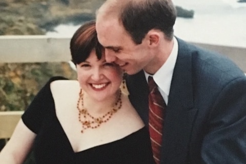 A smiling couple, the woman wears a black dress and the man wears a suit