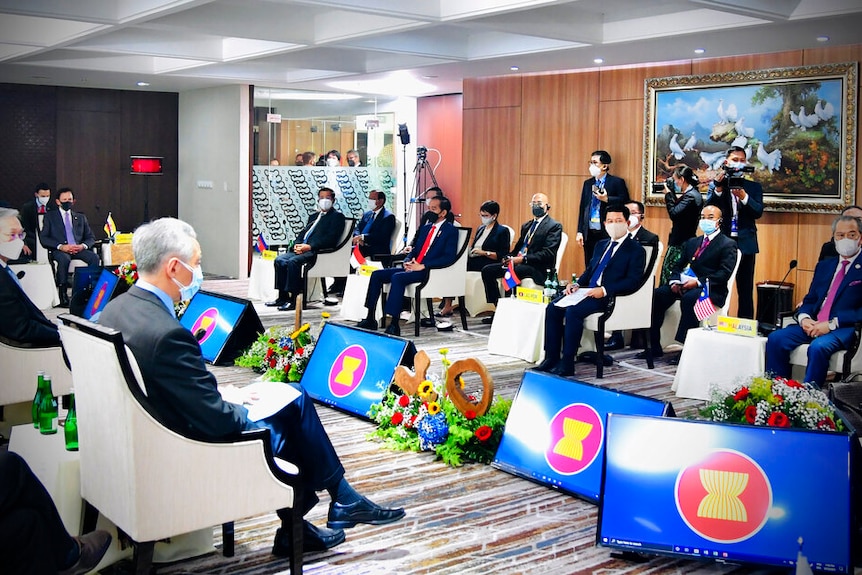 You view a group of men in suits sitting on white armchairs spread around a string of screens showing the ASEAN logo.