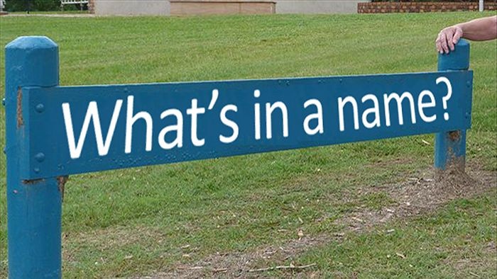 A blue sign with white writing saying what's in a name? with a hand on the corner