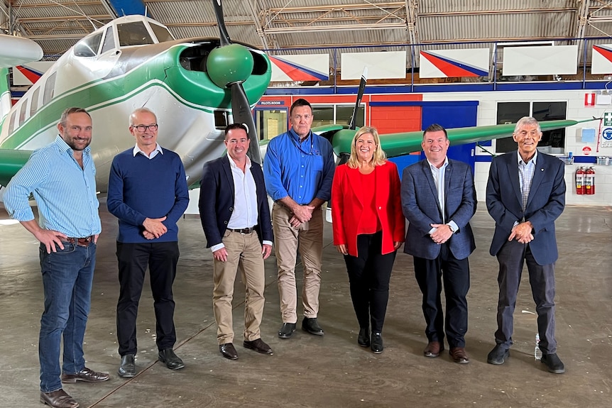 Seven people stand in front of an RFDS plane, smiling.