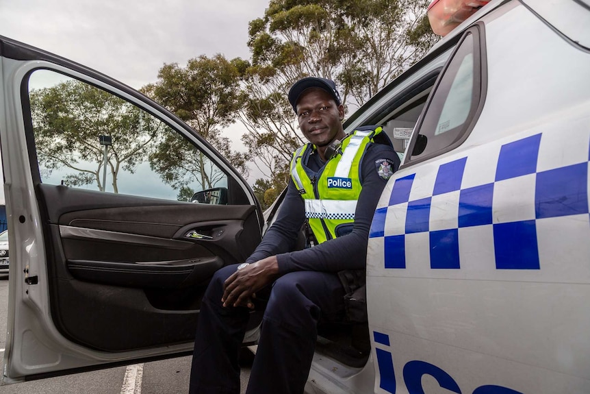 Victoria Police Constable Kur Thiek sitting inside a police car with the door open.