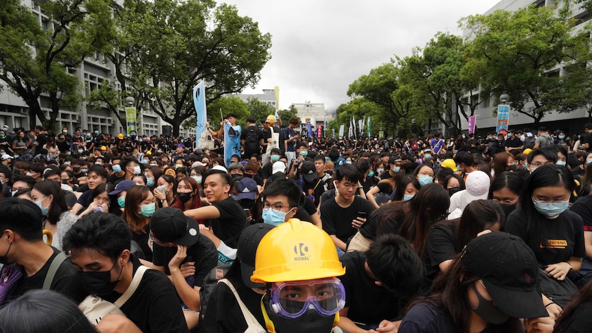A group of hundreds of people wearing black shirts, helmets and face masked.